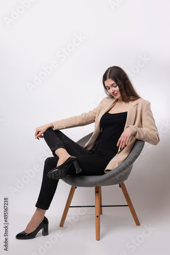 Portrait of a young brunette with long hair in the studio. Cute girl sitting on a chair on a white background.