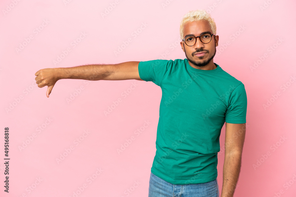 Fototapeta premium Young Colombian handsome man isolated on pink background showing thumb down with negative expression