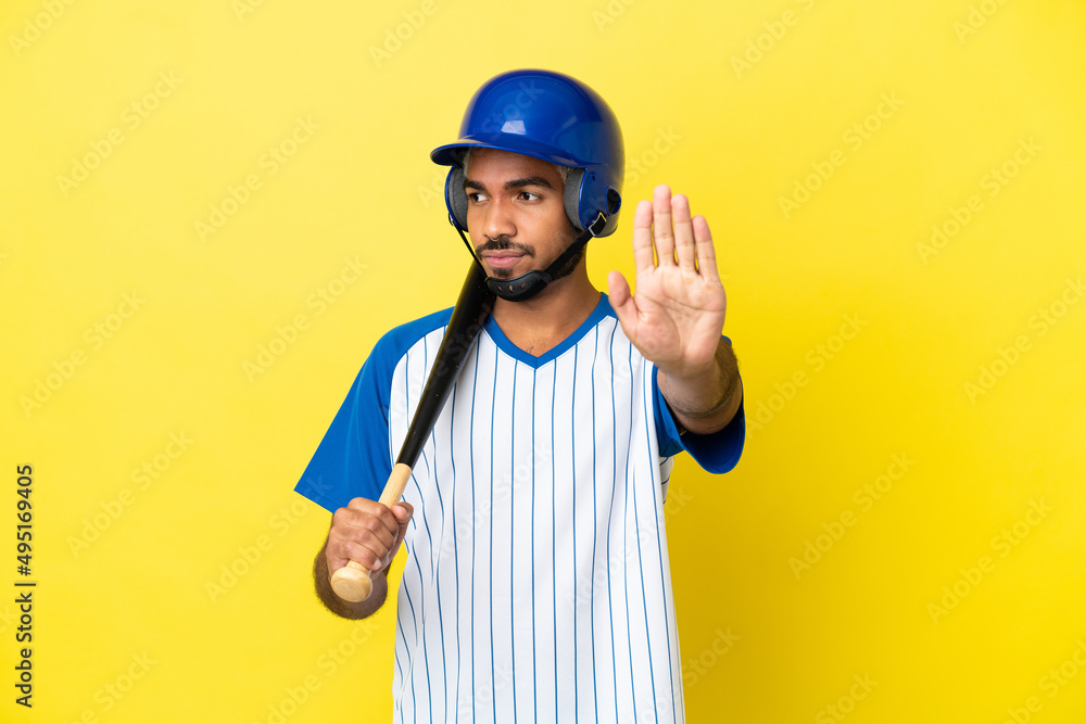 Young Colombian latin man playing baseball isolated on yellow background making stop gesture and disappointed