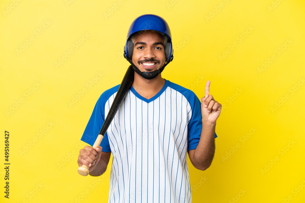 Young Colombian latin man playing baseball isolated on yellow background showing and lifting a finger in sign of the best Young Colombian latin man playing baseball isolated on yellow background showing and lifting a finger in sign of the best