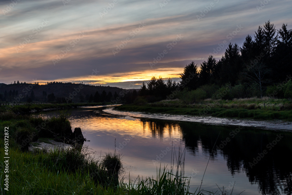 Colorful sunset over the river. Dramatic sky reflects in water. Location is Tillamook River in Oregon, USA