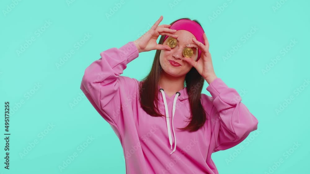 Teenager adult student girl in casual pink hoodie showing golden bitcoins. Achievement career wealth, cryptocurrency investment, mining future technology. Young happy woman on blue studio background Teenager adult student girl in casual pink hoodie showing golden bitcoins. Achievement career wealth, cryptocurrency investment, mining future technology. Young happy woman on blue studio background