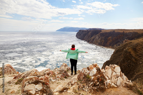 A woman admires the boundless expanses of Lake Baikal. Travel in the spring. White ice floes melt on the water. North of Olkhon Island, Cape Khoboy.