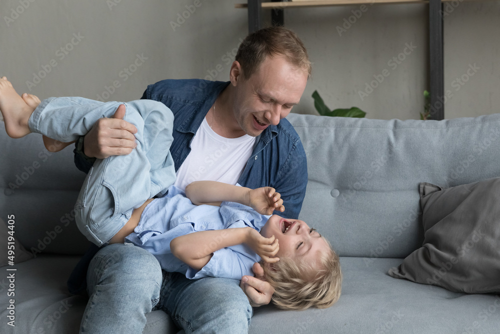 Smiling bonding 35s young father tickling laughing cute little kid son, having fun together on weekend at home, enjoying carefree playtime activity at home, sincere loving family relations concept.