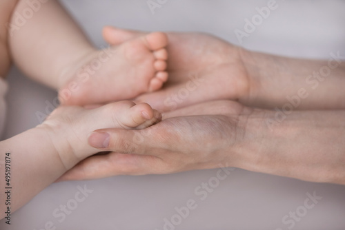 Close up affectionate loving young woman holding in hands tiny cute feet of small newborn baby son daughter, expressing tender caring feelings to few months child indoors, happy motherhood concept.