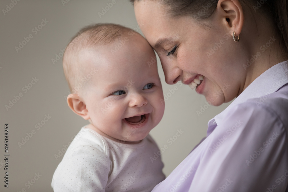 Head shot close up sincere loving millennial mother touching forehead with laughing adorable joyful baby boy girl, expressing candid feelings, enjoying happy motherhood, family devotion concept. Head shot close up sincere loving millennial mother touching forehead with laughing adorable joyful baby boy girl, expressing candid feelings, enjoying happy motherhood, family devotion concept.