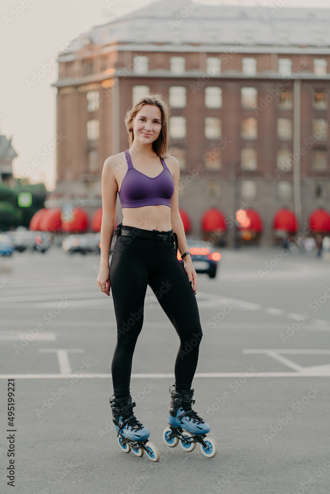 Woman wears cropped top and trousers poses on rollers enjoys free time has healthy body enjoys rollerblading poses outdoor against urban background Woman wears cropped top and trousers poses on rollers enjoys free time has healthy body enjoys rollerblading poses outdoor against urban background