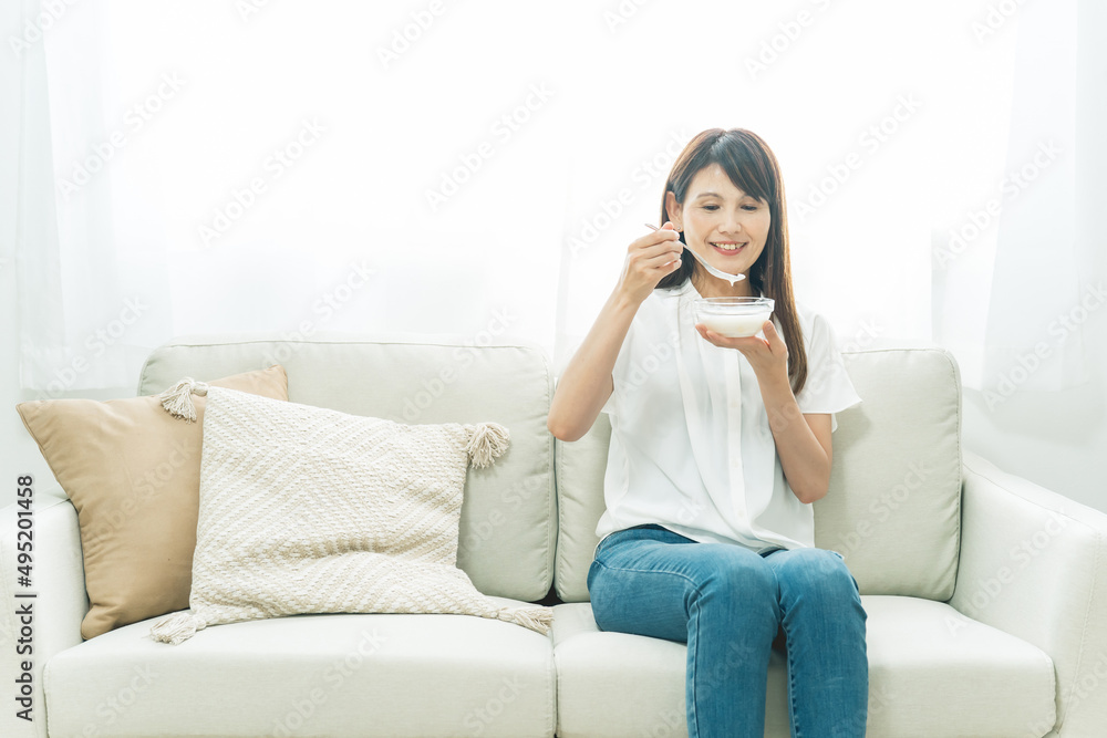ソファでヨーグルトを食べる女性（笑顔）
