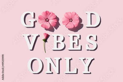 Good vibes only. Motivational quote from white letters and beauty natural flowers on pink background. Creative concept inspirational quote of the day