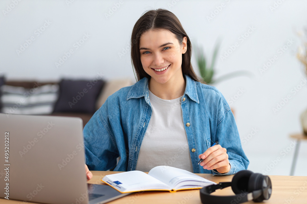 Distance learning, online education. Portrait of smiling young female freelancer working in co-working, modern office or home. Caucasian woman student or employee using laptop computer looking at came