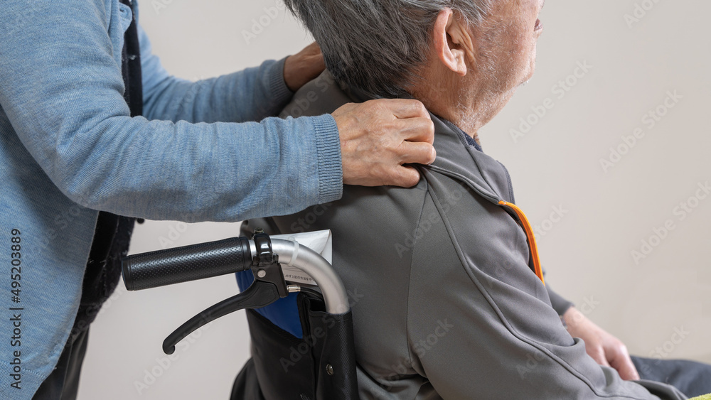 Fototapeta premium 車イスに乗った高齢者旦那の肩に手を置き介護する老人妻