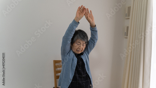 白髪の高齢女性の体操　両手を上に伸ばす