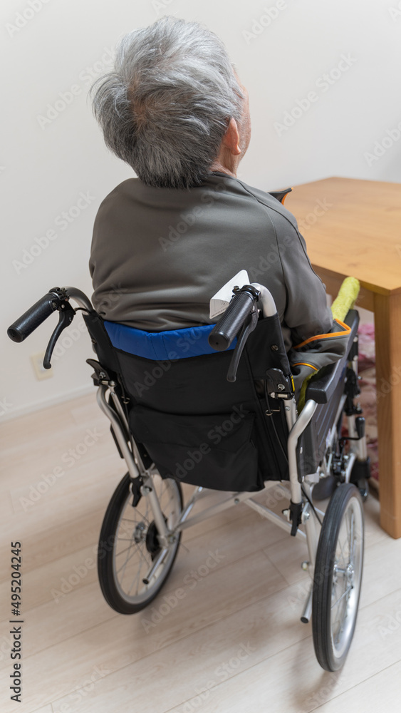 Obraz premium 室内で車イスに乗ってテーブルにつく高齢者男性の後ろ姿