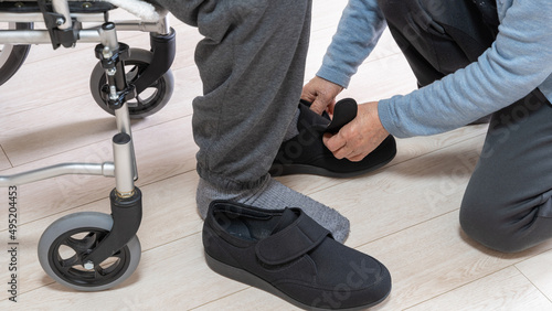 床につけた男性の足に介護シューズをはかせる高齢者女性