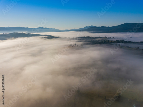 Flight over fog in Ukrainian Carpathians in summer. Mountains on the horizon. A thick layer of fog covers the mountains with a continuous carpet. Aerial drone view.