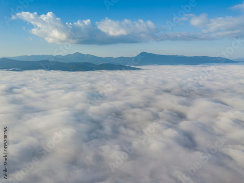 Fototapeta Naklejka Na Ścianę i Meble -  Flight over fog in Ukrainian Carpathians in summer. Mountains on the horizon. A thick layer of fog covers the mountains with a continuous carpet. Aerial drone view.