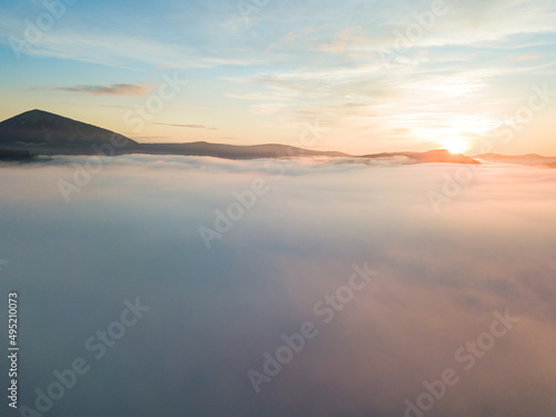 The rays of dawn over the fog in the Ukrainian Carpathians. Aerial drone view.