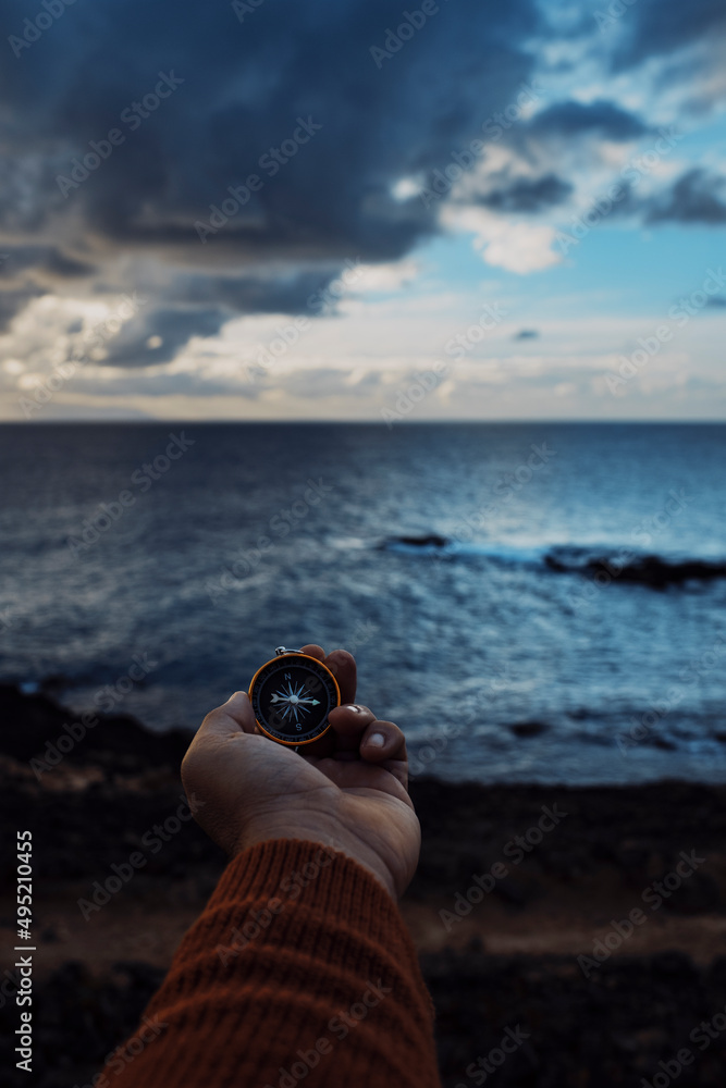 Point of view of man holding navigator compass magnetic. Lost direction and life concept. Caucasian male with compass in front of blue dramatic y and ocean water