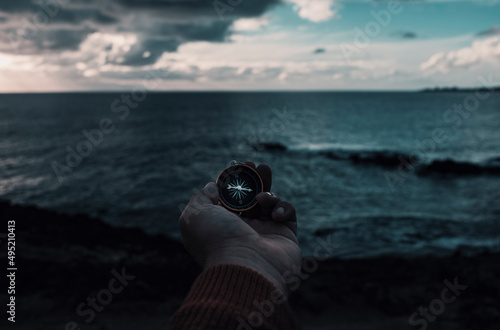 Travel adventure lifestyle concept with man holding navigation compass in front of dramatic sky and ocean landscape. Journey and destination. Lost direction and life. People finding the way