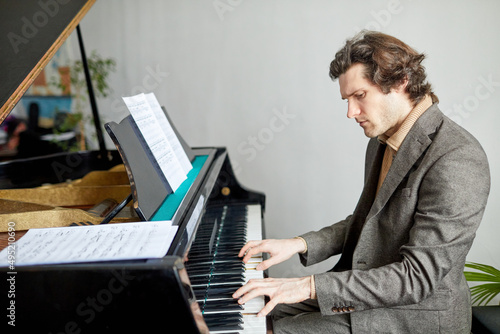 Serious pianist sitting at the piano in front of sheet music and concentrating on his play at lesson