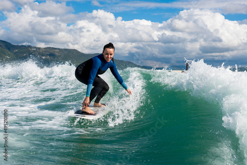 Athletic woman  in wetsuit riding on endless waves behind a boat on sunny day. Female  learning wakesurfing and perfecting tricks. Watersport concept. photo