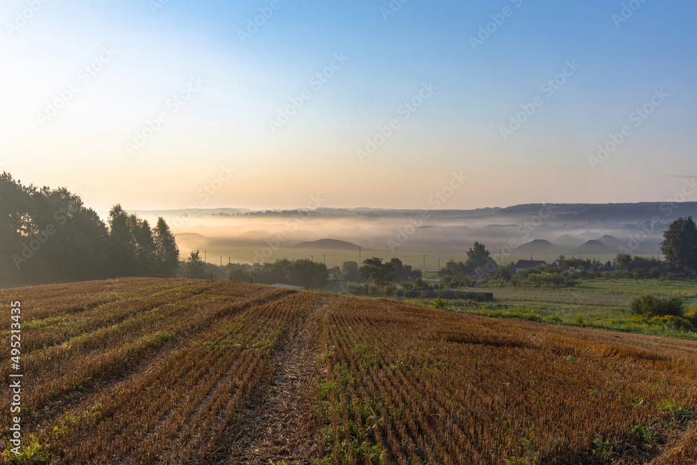 Rural landscape. View from the field to a village in a foggy valley with heaps of mined peat