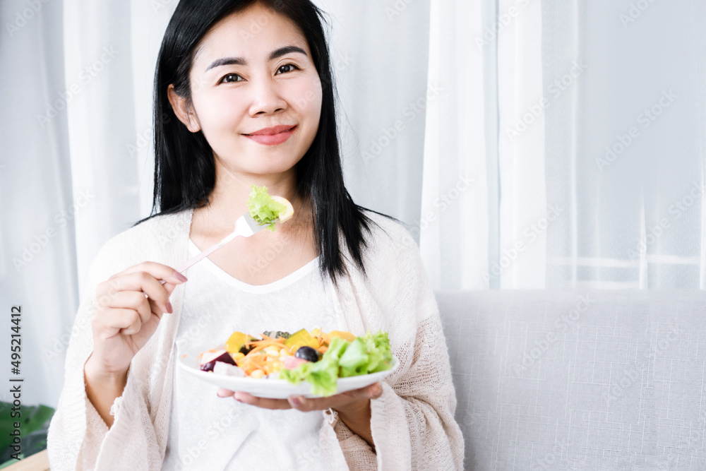 healthy Asian woman eating salad hand holding fork with vegetables in dish healthy Asian woman eating salad hand holding fork with vegetables in dish