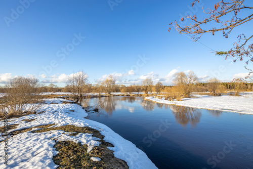March sunny day by the river. A picturesque landscape, early spring, a river with snow-covered banks. The first thaws, the snow is melting.