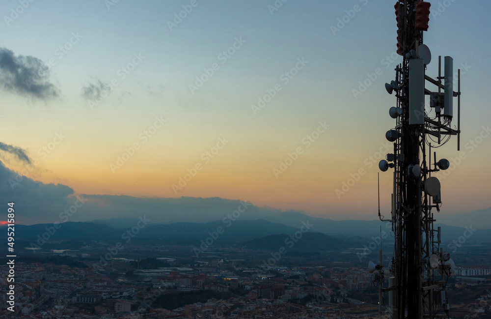 Telecommunications tower with cellular antennas and radar systems. Against the background of the evening sky over the tops of the mountains. Costa Brava, Catalonia
