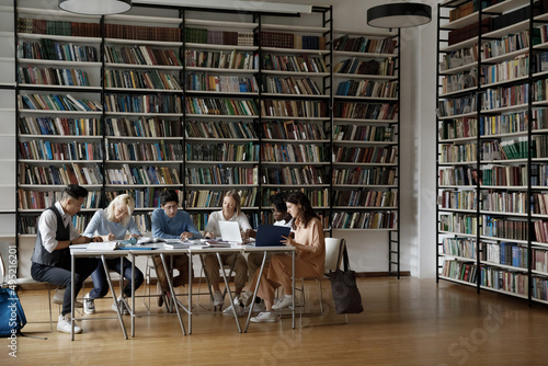 Group of multi racial students sit at table in spacious room of high school library, doing assignment, prepare for exams or admission looking focused. University education, studying process concept