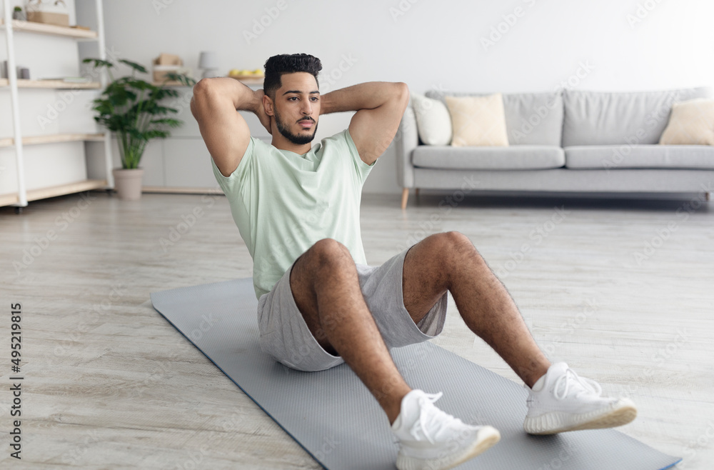 Fototapeta premium Handsome young Arab man exercising on yoga mat, strengthening abs muscles at home, copy space
