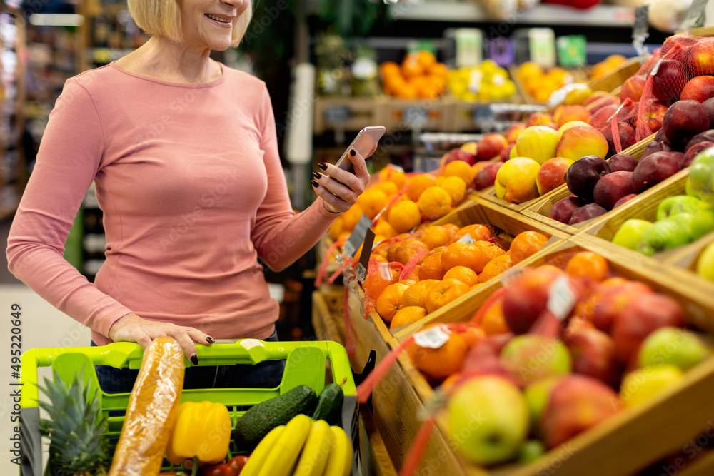 Cropped of senior woman using smartphone while shopping at supermarket