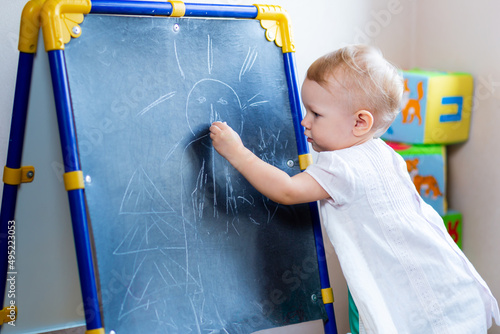 Photography cute little female artist paints on an easel with chalk while standing on a chair