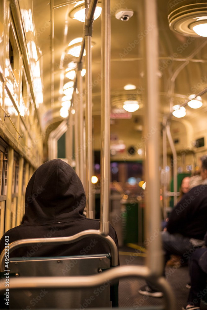 A men with his hood on his head inside a bus at night sitting alone. A retro bus with circular lights. Nighttime. Lonely hooded man in a bus.