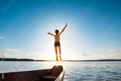 Little boy jumps into the water from a wooden boat at sunset. Happy summer vacation near the sea concept.