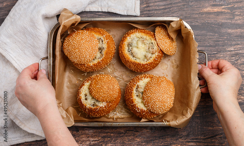 In women's hands baking sheet with Julienne in sesame buns. Bread roll baked with cheese, mushrooms, chicken and bechamel sauce. Delicious homemade breakfast, lunch or dinner