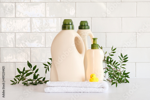Eco friendly organic natural baby laundry detergent container and soap gel bottle with branch of green leaves, towel and yellow duck on table in bathroom. photo