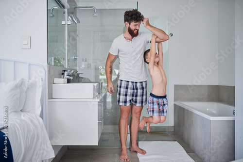 Dads got super strength. Shot of a little boy hanging on his fathers arm in the bathroom at home.