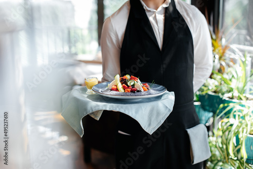 Close-up of a young waiter in a stylish uniform carrying an exquisite salad to a client in a beautiful gourmet restaurant. Table service in the restaurant. photo