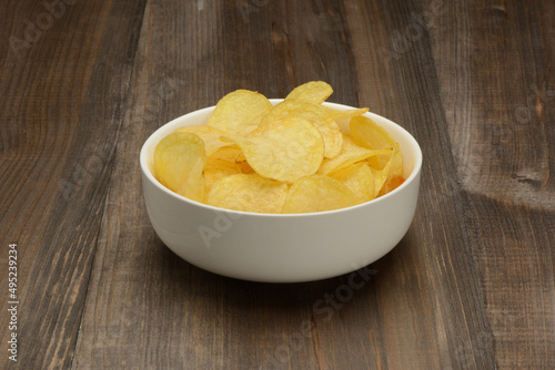 Patatas fritas o chips en un bol de cerámica blanca sobre fondo la mesa marrón