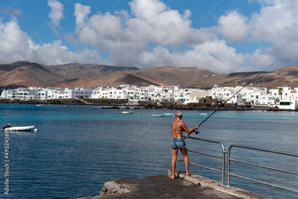 Una mujer rubia de espaldas pescando en la costa de Lanzarote en las Islas Canarias. Turismo de pesca. Pueblo de Punta mujeres. 