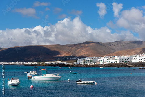 costa de Punta Mujeres en Lanzarote en las Islas Canarias. Yate y barcos varados en un mar turquesa con casa blancas de fondo y montes volcánicos. Naturaleza y paisaje canario. © Safi