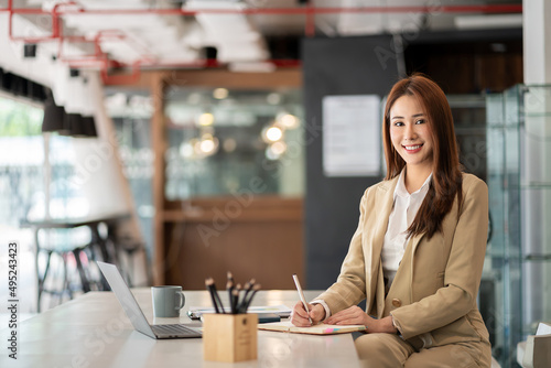 Smiling beautiful Asian businesswoman working on laptop and documents in financial accounting concept office