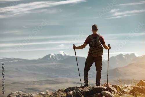 Tourist with backpack and hiking poles stands in mountains and looks at the view