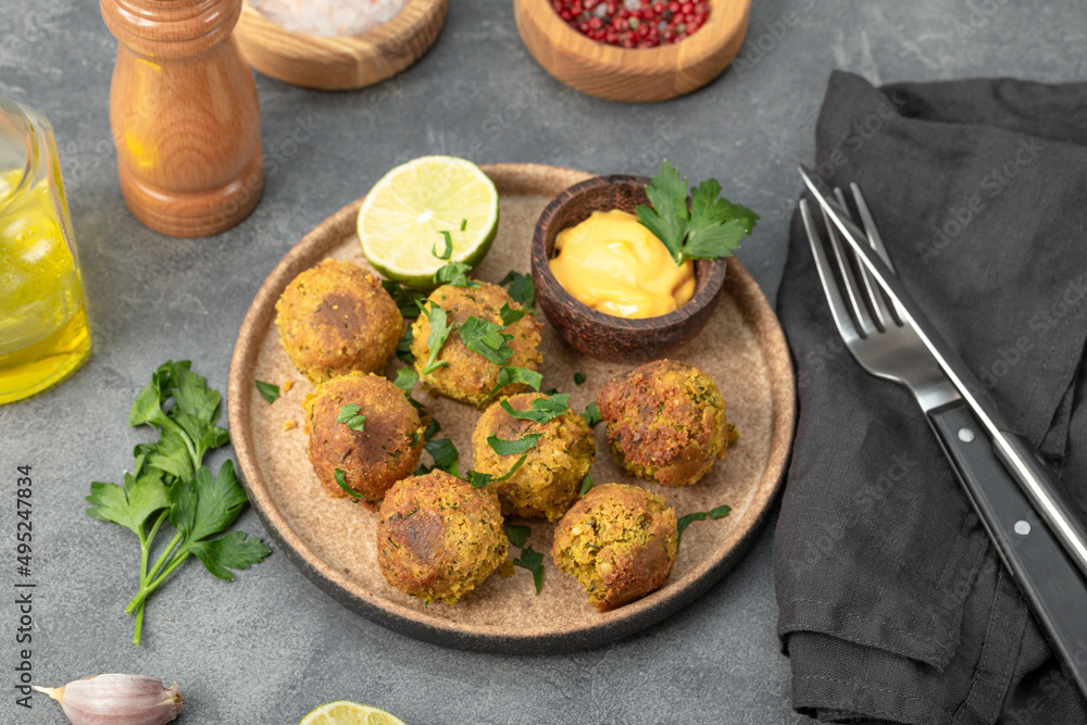 Chickpea falafel with lime and sauce on a plate and grey table