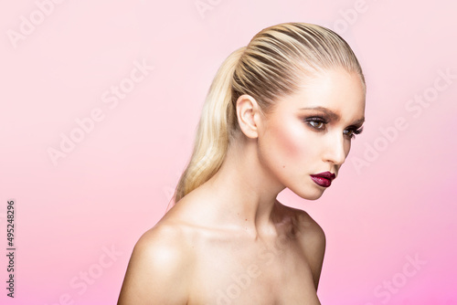 Closeup portrait of young woman with beautiful makeup and hair straightened and caught in the back, pink background.
