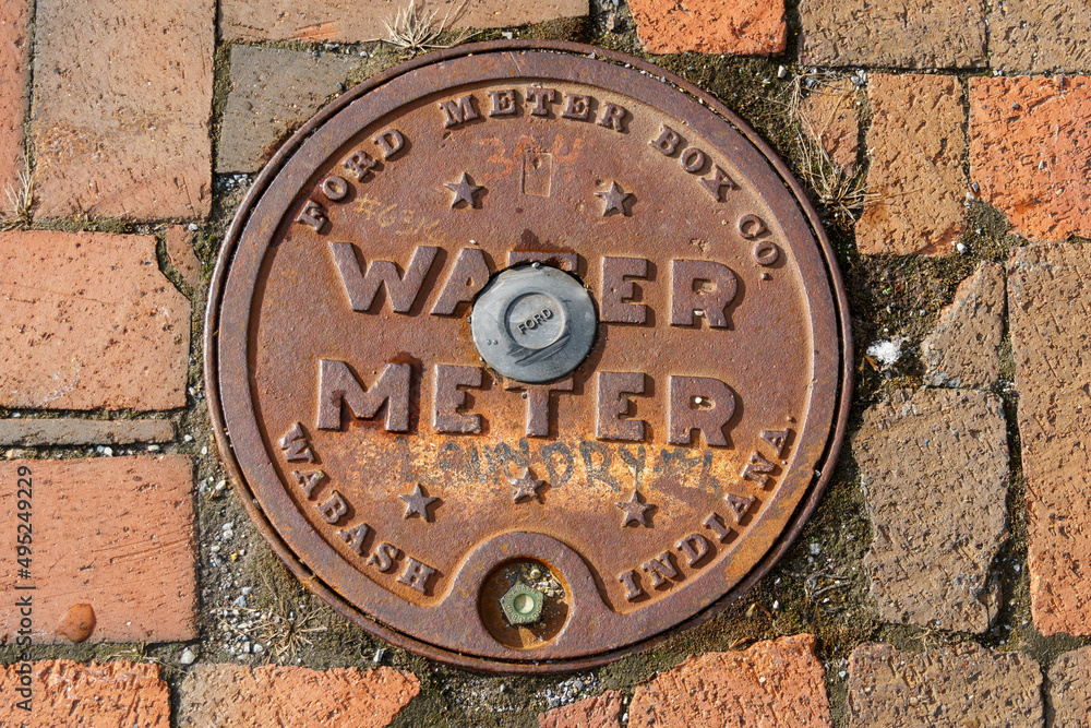 Rusted water meter access hatch on a brick street
