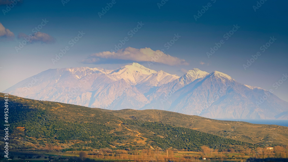 View of the highest snowy mountain of Samothrace island from the center of Gökçeada, Turkey. Greenery and sea view along the valley.
