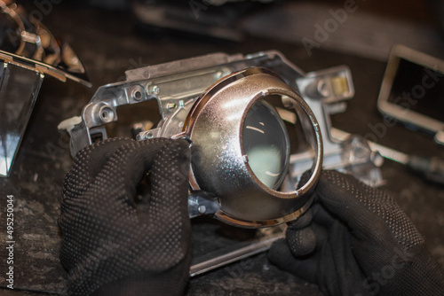 A mechanic in black gloves installs an LED lens into the headlight housing.Car headlight during repair and cleaning.The mechanic restores the headlight of the car.Restoration of automotive optics. photo