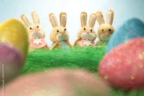Four cute easter bunnies behind colorful easter eggs against a light blue background.